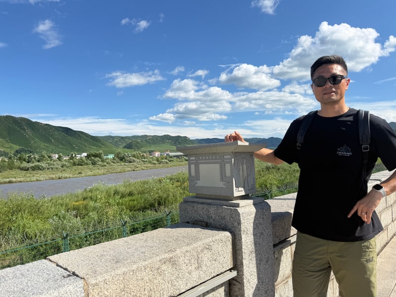 胡俊在户外旅行中的个人照片，身后是河流与远山